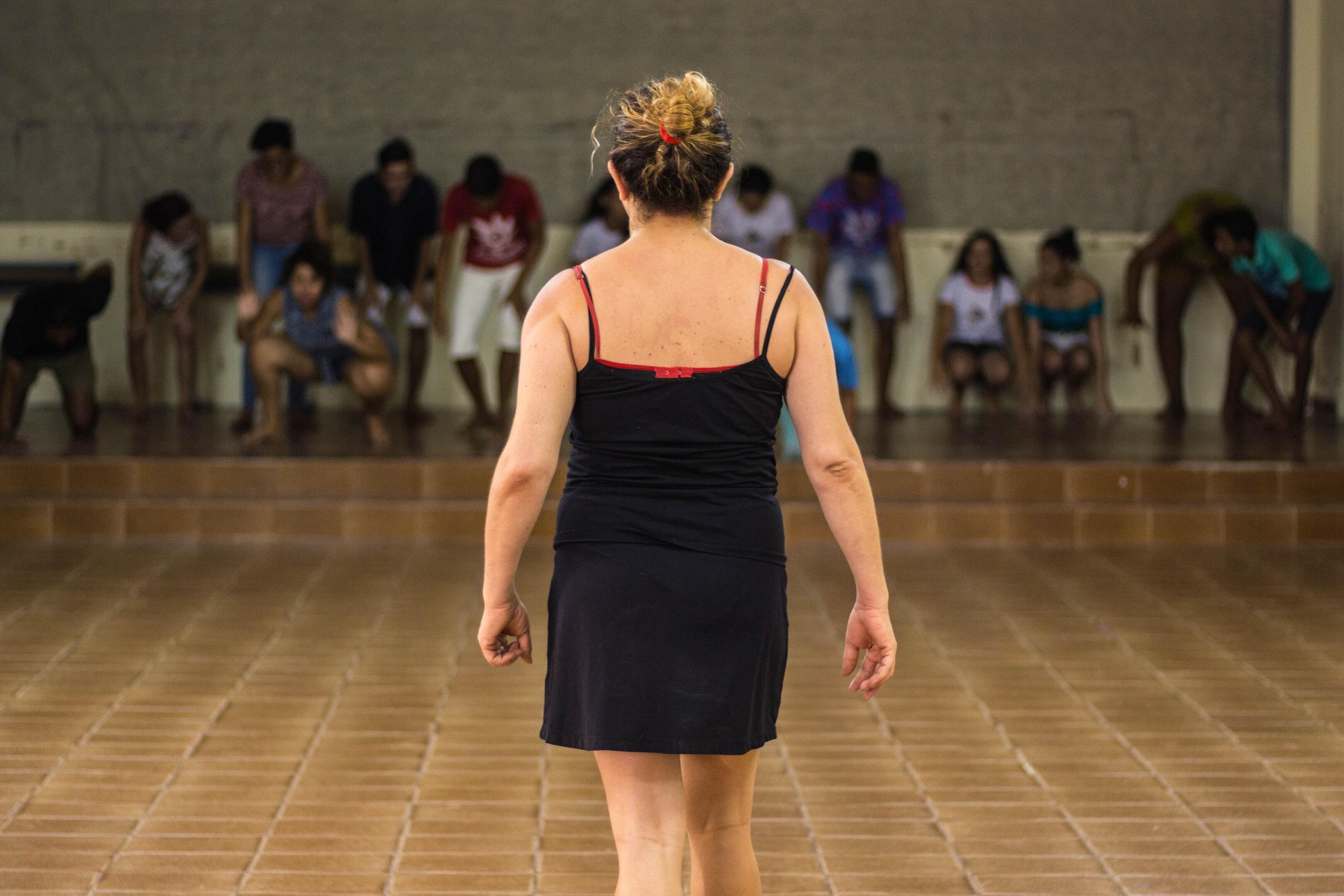 imagem de Suzy Lopes de costas e ao fundo seus alunos na oficina de teatro agachados, se preparando para correr