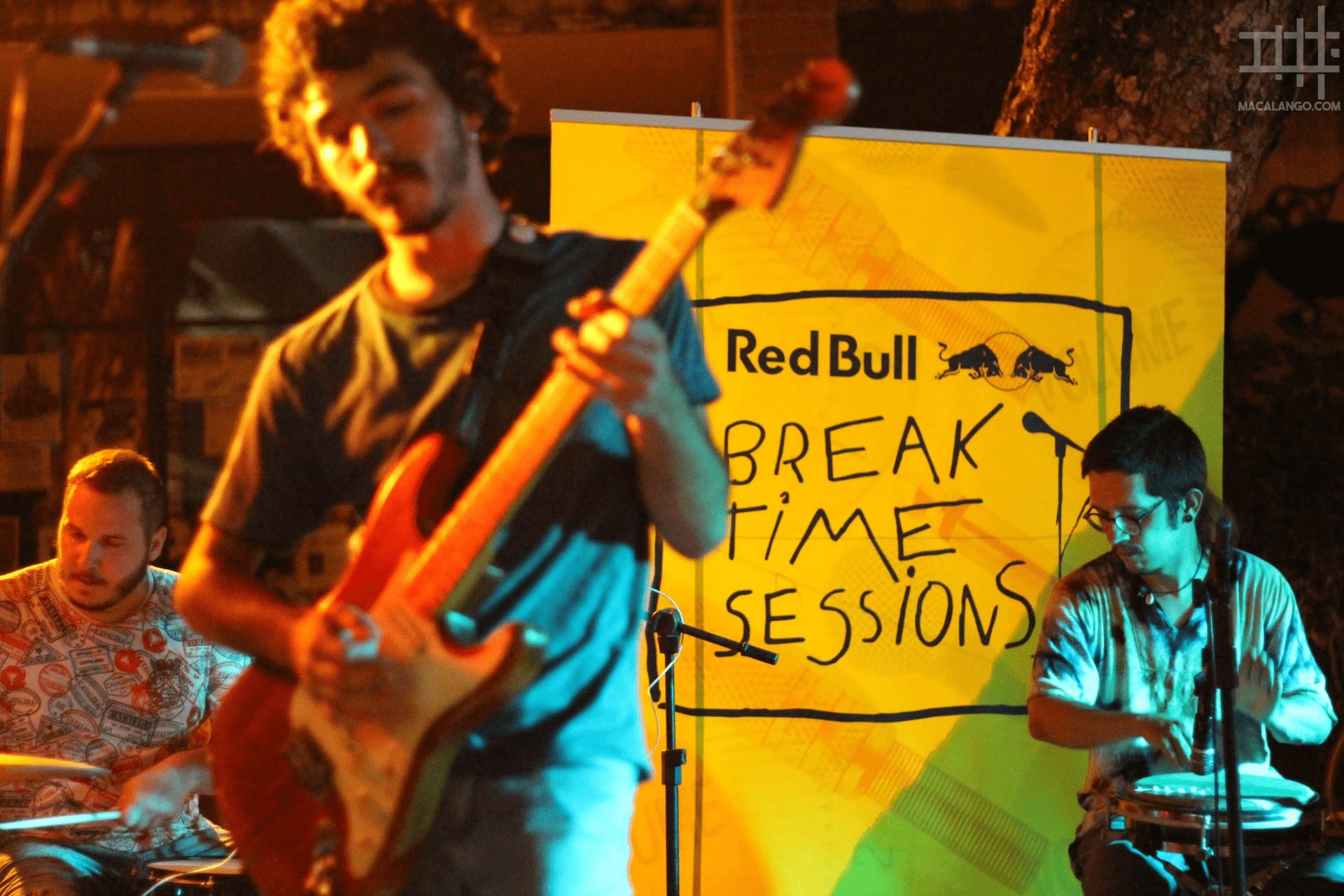 foto do baterista, guitarrista e percussionista com banner do evento escrito RED BULL BREAKTIME SESSIONS